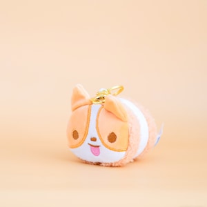 May include: A plush peach-coloured dog keyring with a white stripe and a pink tongue sticking out. The keyring has a gold metal ring.