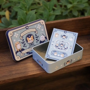 May include: A light blue metal tin and a card featuring a corgi illustration. The tin has a decorative design with the text "THOUSANDSKIES" and "MYSTERY". The card inside the tin has a similar design with corgi illustrations.