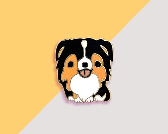 May include: A black, brown, and white enamel pin of an Australian Shepherd dog with its tongue sticking out.
