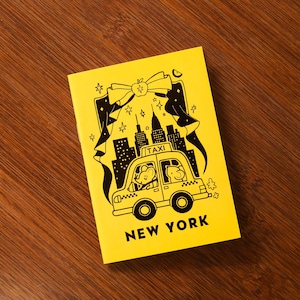 May include: A bright yellow rectangular notebook featuring a black line art illustration of a taxi cab with two mouse characters inside, a city skyline, a large bow, and stars. The text "TAXI" is on the roof and "NEW YORK" is printed at the bottom.