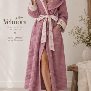 May include: A dusty rose waffle-textured robe featuring a hood and cuffs lined with a cream-colored fabric adorned with a delicate pink floral pattern. The robe includes a matching floral tie belt and two front pockets. Text reads Velmora.