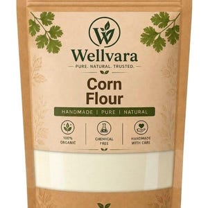 Op de afbeelding: Een bruine papieren zak met maïsmeel en een doorzichtig venster aan de onderkant. Het etiket bevat de tekst Wellvara, Pure. Natural. Trusted., Corn Flour, Handmade | Pure | Natural, 100% Organic, Chemical Free, Handmade With Care.