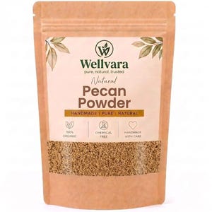 Peut inclure: Un sachet en papier brun contenant de la poudre de noix de pécan. L'étiquette porte le texte Wellvara, Natural Pecan Powder, Handmade, Pure, Natural, 100% Organic, Chemical Free, et Handmade With Care, avec des icônes de feuilles et de cœur.