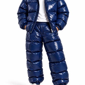 May include: A glossy navy blue puffer jacket and matching puffer pants set. The jacket features a high collar and a full-length front zipper. The pants have an elasticized waistband and cuffs. A plain white t-shirt is worn underneath the jacket.