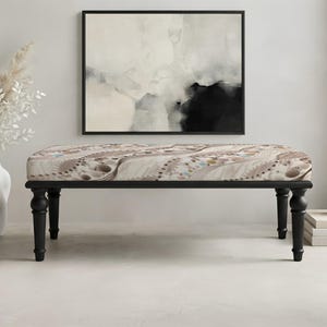 May include: A rectangular bench featuring four black turned wooden legs and a cushioned seat upholstered in a fabric with a beige, brown, and cream abstract pattern consisting of swirling lines and small circular dot motifs across the surface.