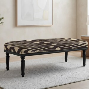 May include: A rectangular upholstered bench featuring a dark brown and cream abstract wavy pattern on the seat. The bench is supported by four black turned wooden legs that provide a stable base for the cushioned top surface.