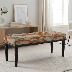 May include: A rectangular bench featuring a cushioned seat with a marbled pattern in shades of burnt orange and cream. The bench is supported by four black, turned wooden legs that provide a stable base for the upholstered top surface.