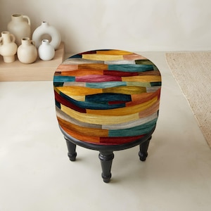 May include: A round ottoman featuring a vibrant, multi-colored pattern of horizontal, wood-grain textured segments in shades of deep blue, mustard yellow, terracotta red, and soft beige, supported by four short, dark-finished turned wooden legs.