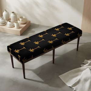 May include: A rectangular bench featuring a black upholstered seat with a repeating gold palm tree pattern. The bench is supported by four slender, dark brown wooden legs that taper toward the floor, providing a stable base for the seat.