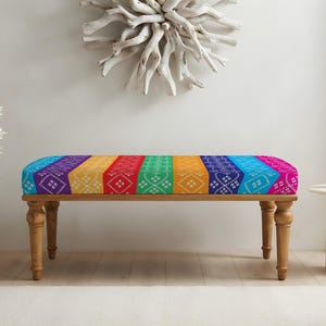 May include: A rectangular bench with four turned wooden legs and a cushioned seat upholstered in a vibrant, multi-colored fabric featuring vertical stripes of purple, yellow, red, green, orange, blue, and pink with a repeating white geometric pattern.