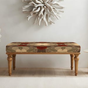 May include: A rectangular bench with four turned wooden legs and a cushioned seat featuring a repeating geometric pattern in shades of deep red, muted olive green, and cream. The upholstery displays a symmetrical design with floral-like motifs.