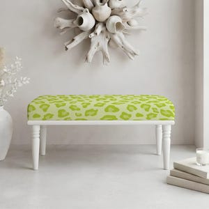 May include: A rectangular bench featuring a lime green and light green leopard print pattern on the upholstered seat, supported by four white turned wooden legs. The bench has a clean, structured design with a flat top and tapered legs.