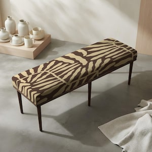 May include: A rectangular bench featuring a dark brown and beige abstract organic pattern on the upholstered seat. The bench is supported by four slender, dark brown wooden legs that taper toward the floor, providing a stable base for the seat.