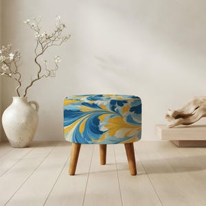 May include: A round ottoman featuring a vibrant marbled pattern in shades of blue, yellow, and white. The seat is supported by three tapered wooden legs in a light brown finish, providing a stable base for this functional piece of furniture.