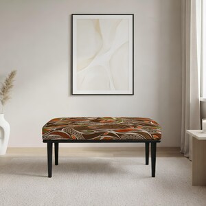 May include: A rectangular bench featuring a cushioned seat upholstered in a fabric with a complex, swirling pattern in shades of brown, orange, olive green, and cream. The bench is supported by four straight, black, tapered wooden legs.
