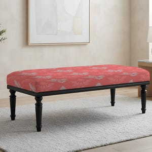 May include: A rectangular upholstered bench featuring a coral-colored fabric with a repeating light gray floral pattern. The bench is supported by four turned black wooden legs that provide a stable base for the cushioned seat top.