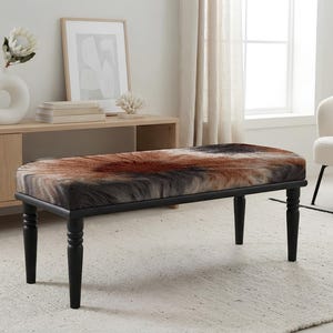 May include: A rectangular bench featuring a textured, faux-fur seat with a radial pattern in shades of brown, black, and cream. The bench is supported by four slender, turned wooden legs finished in a matte black paint, providing a stable base.