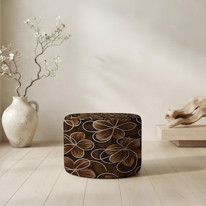 May include: A cylindrical ottoman featuring a dark brown background with a repeating pattern of light brown and white line-drawn flowers. The piece has a smooth, rounded top and straight sides, showcasing a consistent floral graphic design.