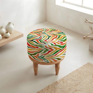 May include: A round ottoman featuring a vibrant, multi-colored zebra stripe pattern in shades of red, orange, yellow, and green. The seat is supported by four short, light-toned wooden legs with a turned, tapered design that provides stability.