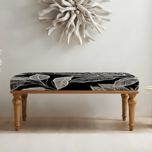 May include: A rectangular bench featuring a black upholstered seat with a white line-drawn botanical leaf pattern. The bench is supported by four turned wooden legs with a natural light brown finish, providing a stable base for the seat.