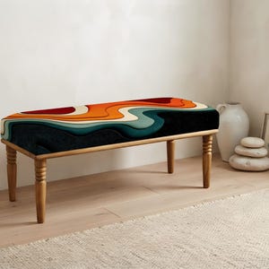 May include: A rectangular bench featuring four light-toned wooden legs with a turned design. The upholstered seat displays a layered, wavy pattern in shades of deep red, bright orange, cream, light teal, and dark charcoal gray across the top.