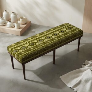 May include: A rectangular bench featuring a green fabric seat with a repeating geometric diamond pattern in white and dark brown. The bench is supported by four slender, dark brown wooden legs that taper toward the floor.