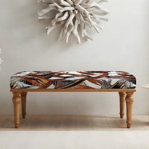 May include: A rectangular bench featuring four turned wooden legs and a cushioned seat upholstered in a fabric with an abstract pattern of black, white, and burnt orange brushstrokes. The bench has a natural wood finish on the base.