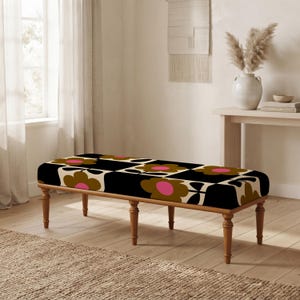 May include: A rectangular bench with four turned wooden legs and a cushioned seat featuring a repeating pattern of large brown flowers with bright pink centers on a black background. The bench has a low profile and a sturdy wooden frame.