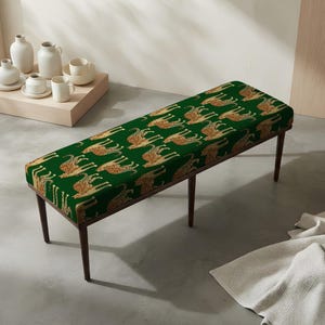 May include: A rectangular bench featuring a deep green upholstered seat with a repeating pattern of golden-brown cheetahs. The bench is supported by four slender, dark brown wooden legs that angle outward, providing a stable base for the seat.