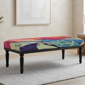 May include: A rectangular bench featuring a cushioned seat upholstered in a vibrant, multi-colored abstract pattern with shades of pink, orange, blue, and light green. The bench is supported by four turned, black wooden legs.
