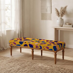 May include: A rectangular bench featuring a mustard yellow upholstered seat with an abstract pattern of blue, purple, and pink brushstroke shapes. The bench is supported by six turned wooden legs with a medium brown finish and a tapered design.