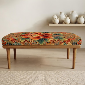 May include: A rectangular bench with four light brown wooden legs and a cushioned seat featuring a vibrant, intricate pattern of large red and orange flowers, green leaves, and swirling blue and gold geometric motifs on a dark background.