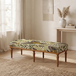 May include: A rectangular upholstered bench featuring a botanical pattern with green leaves, yellow flowers, and dark grey bird illustrations. The bench is supported by six turned wooden legs in a medium brown finish, providing a stable base.