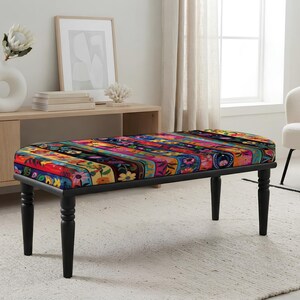 May include: A rectangular bench featuring a seat upholstered in a vibrant, multi-colored fabric with a dense floral and striped pattern. The bench is supported by four black, turned wooden legs that provide a sturdy base for the cushioned seat.