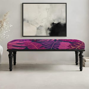 May include: A rectangular bench featuring a dark navy blue and vibrant magenta tropical leaf pattern on the upholstered seat. The bench is supported by four black turned wooden legs, providing a stable base for the cushioned top surface.
