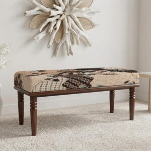 May include: A rectangular bench featuring four dark brown wooden legs with turned detailing. The seat is upholstered in a beige fabric decorated with a repeating dark brown and black geometric pattern, accented by small teal floral motifs.