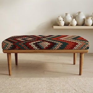 May include: A rectangular bench with four light-toned wooden legs and a cushioned seat featuring a repeating geometric pattern in shades of dark red, teal, cream, and brown, resembling a knit texture with chevron and diamond shapes.