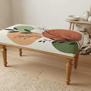 May include: A rectangular upholstered bench with four turned wooden legs. The seat features a cream-colored fabric printed with abstract shapes in muted green and terracotta, accented by black line-drawn botanical leaf patterns and white dots.