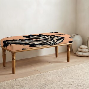 May include: A rectangular bench featuring a peach-colored upholstered seat with a bold, black and white abstract feather-like pattern. The bench is supported by four turned wooden legs with a natural light brown finish and a smooth texture.