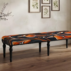 May include: A long rectangular bench featuring a dark charcoal gray fabric seat with a vibrant orange and white abstract floral pattern. The bench is supported by four turned black wooden legs, providing a stable base for the upholstered top.