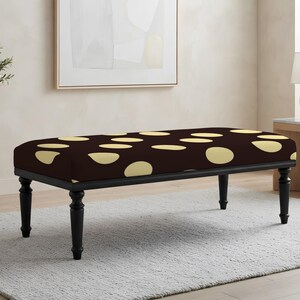 May include: A rectangular bench featuring a dark brown upholstered top with a pattern of light yellow, irregular circular spots. The bench is supported by four black, turned wooden legs that provide a stable base for the cushioned seat.