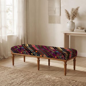 May include: A rectangular upholstered bench featuring a vibrant, multi-colored fabric with diagonal stripes of floral and geometric patterns in shades of deep purple, red, orange, and gold, supported by four turned wooden legs in a light brown finish.