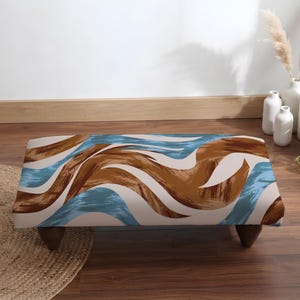 May include: A rectangular ottoman featuring a wavy, abstract pattern in shades of brown, light blue, and cream. The piece is supported by four dark brown, tapered wooden legs, providing a stable base for this low-profile furniture item.