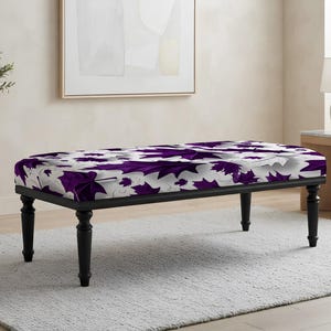May include: A rectangular bench featuring a cushioned top upholstered in a white fabric with a repeating pattern of deep purple maple leaves. The bench is supported by four black, turned wooden legs that provide a stable base for the seat.