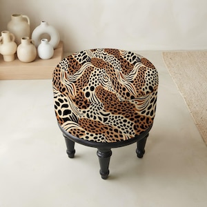 May include: A round ottoman featuring a bold animal print pattern in shades of brown, black, and cream. The seat is upholstered in fabric with a leopard-inspired design and is supported by four short, turned legs finished in a solid black color.