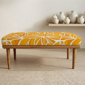 May include: A rectangular bench featuring a vibrant orange and white floral pattern on the upholstered seat. The bench is supported by four light-toned wooden legs that extend outward from the base, providing a stable foundation for the seat.