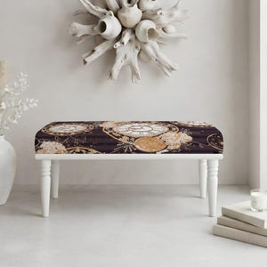 May include: A rectangular bench featuring four white turned legs and a cushioned seat upholstered in a dark fabric with a repeating pattern of gold and white vintage pocket watch faces, clock gears, and soft floral accents in shades of cream.