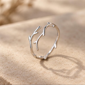 May include: A silver-toned ring featuring an open design that mimics the appearance of thin, branching twigs. The metal band is polished and smooth, with small, protruding nodes along the structure that resemble natural tree branch growth.