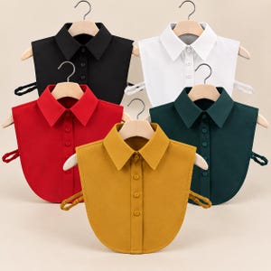 May include: A collection of five detachable shirt collars in black, white, red, dark green, and mustard yellow. Each collar features a pointed collar design, a front button placket with matching buttons, and adjustable side straps for a secure fit.
