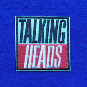 以下が含まれることがあります： TALKING HEADSという文字が刺繍された長方形のワッペン。上半分は水色の背景に黒い文字、下半分は赤い背景に白い文字が配置されており、全体が細い黒い枠で囲まれています。
